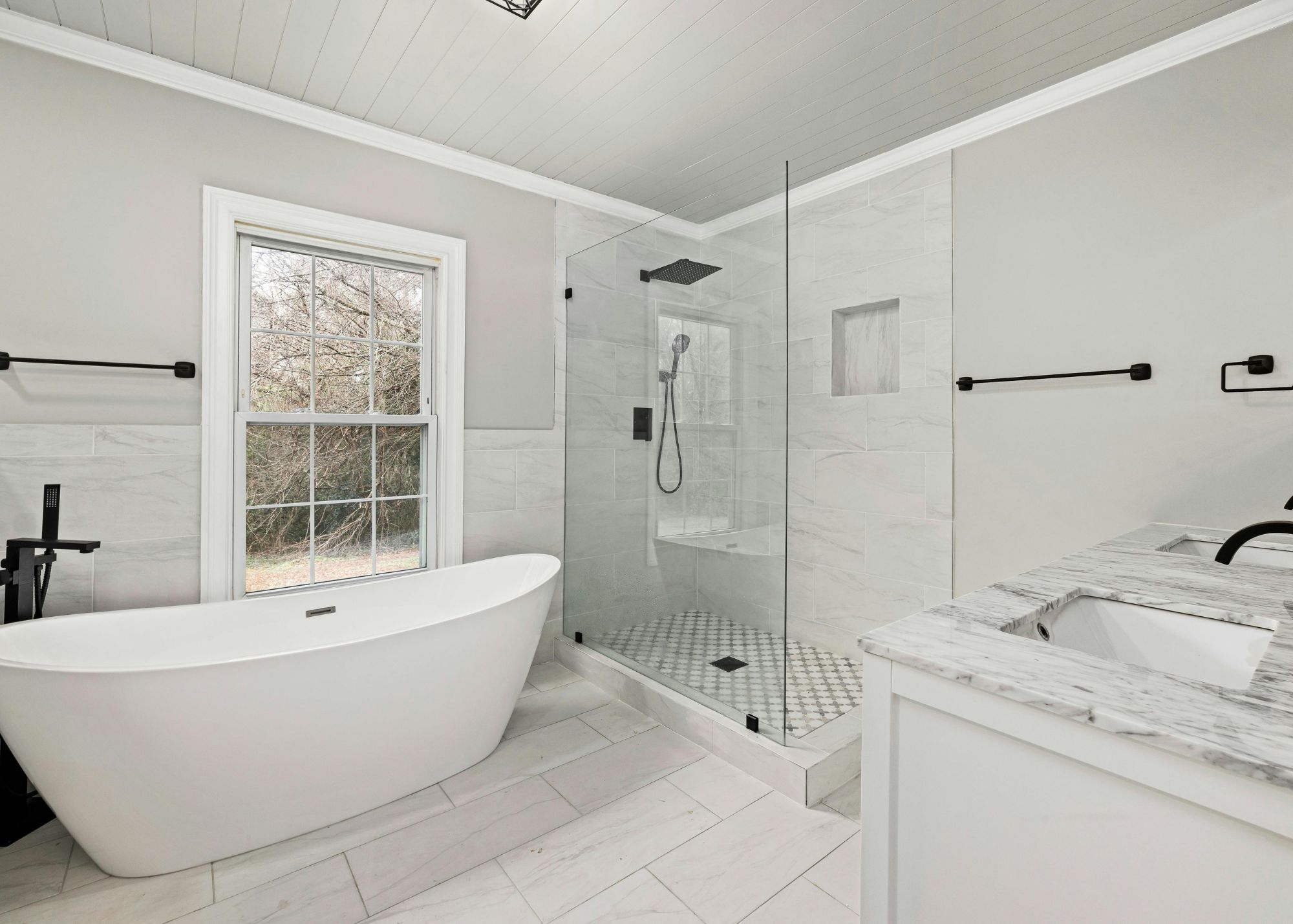 Modern bathroom remodel with freestanding tub, marble tile, and glass shower
